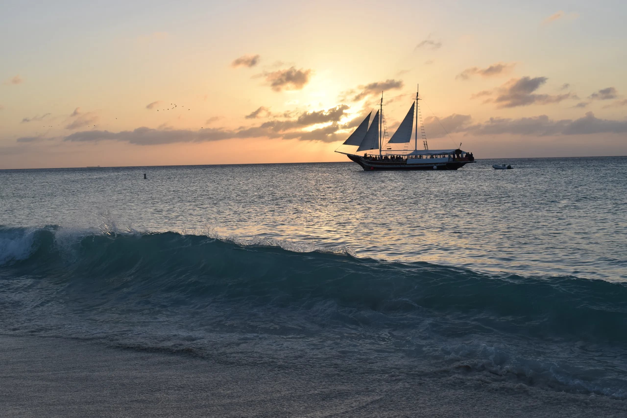 A tall ship under full sail on a calm sea at golden sunset